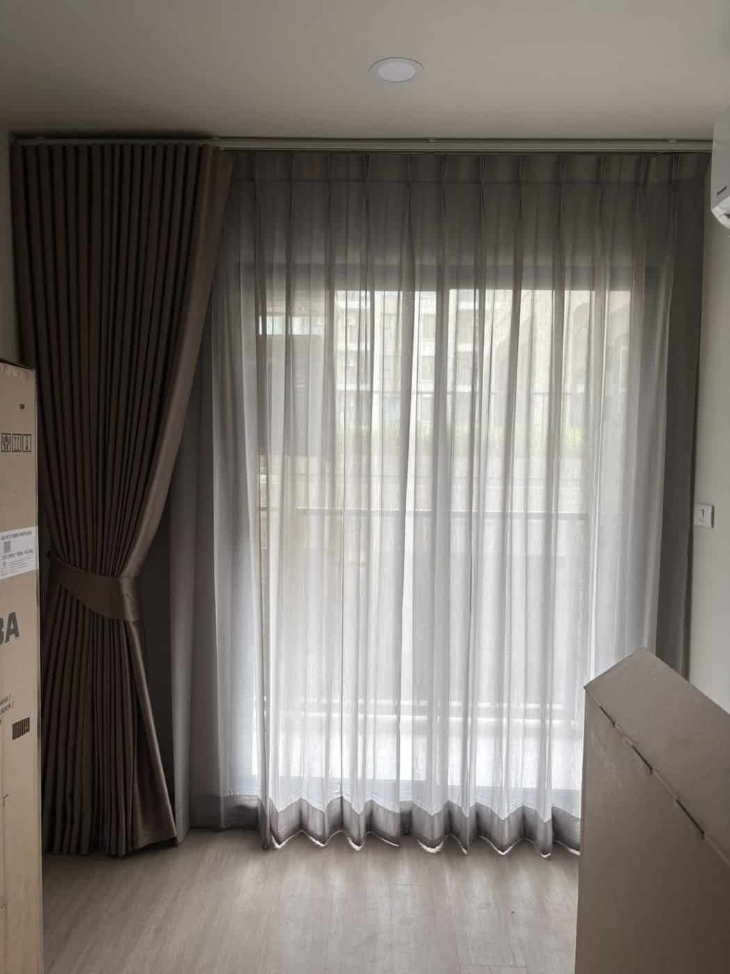 Brown drapes with tiebacks and sheers puddling on the floor beside a tall window