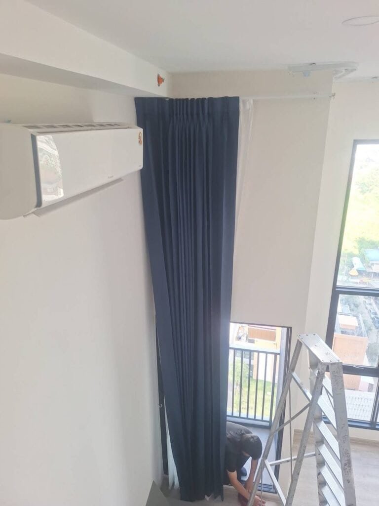 Installer fitting a navy pinch pleat curtain with sheer underlayer on a double-height window and ceiling track