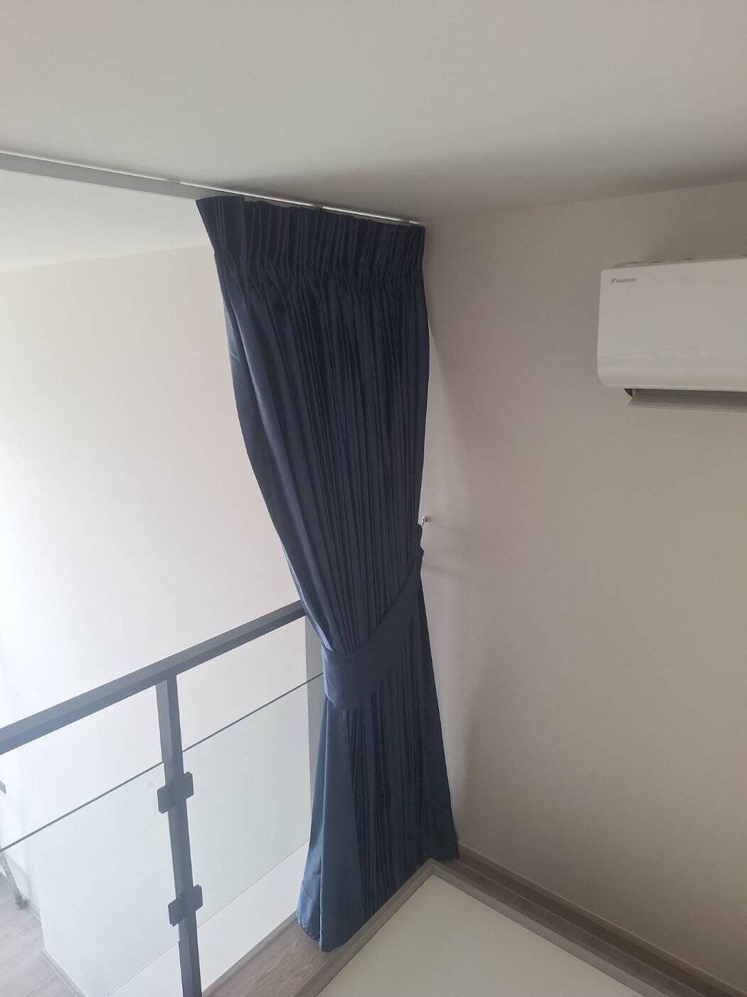 Navy pinch pleat curtain with fabric tieback on a tall loft window