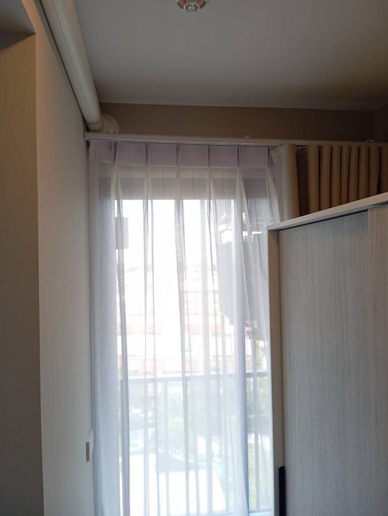Close-up of pinch pleat sheer heading and gliders on a white ceiling-mounted curtain track